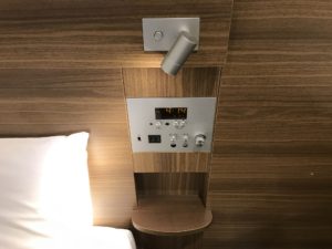 京王プレッソイン浜松町 シングルルーム 枕元 目覚まし時計とスイッチ類、コンセント、USBポートがあります