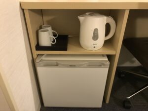 スーパーホテル 東京・芝 シングルルーム デスク左下 マグカップ、電子ケトル、冷蔵庫があります