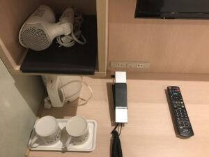相鉄フレッサイン東京田町 ダブルルーム デスク左 ACコンセントとLANコネクタ、ドライヤ、鏡、電気ケトル、マグカップ、電話機があります