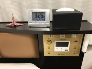 アパホテル 上野駅前 スタンダードルーム 枕元 目覚まし時計とACコンセント、USBポート、エアコン・明かりのスイッチ、非常灯があります