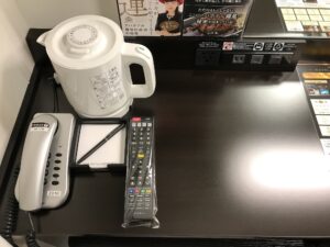 アパホテル 上野駅前 スタンダードルーム デスク回り 左側に電話機と電気ポット、テレビのリモコンがあります