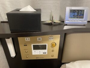 アパホテル 秋葉原駅東 スタンダードルーム 枕元 目覚まし時計とACコンセント、USBポート、照明とエアコンのスイッチ、ティッシュ、非常灯があります