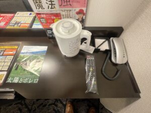 アパホテル 秋葉原駅東 スタンダードルーム デスク回り ACコンセントと有線LAN、電気ポット、テレビのリモコン、メモ、電話があります
