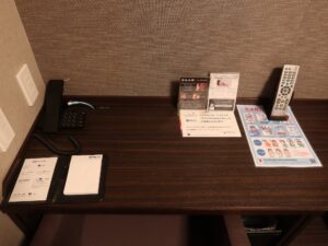 ドーミーイン鹿児島 ダブルルーム デスク回り 電話とLANケーブル、メモ、テレビのリモコンがあります
