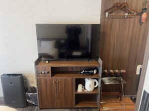 熊谷天然温泉 ハナホテル籠原 シングルルーム テレビ、キャビネット、加湿空気清浄機、ごみ箱、ハンガー キャビネットにはドライヤーと電気ポット、マグカップがあります